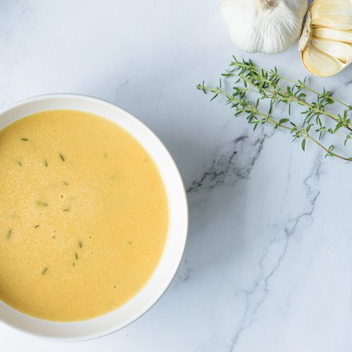 Een romige knoflooksoep in een witte kom, gegarneerd met verse tijm. Een eenvoudig en smaakvol gerecht met aardappel, kippenbouillon en olijfolie