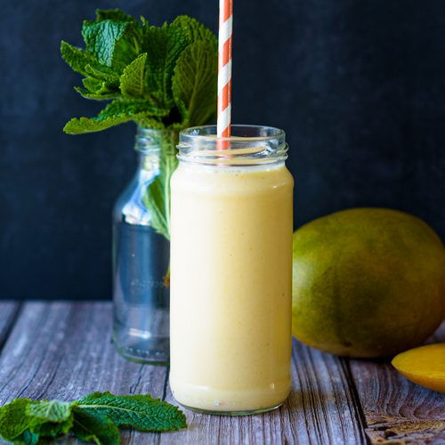 Een frisse mango-nectarine smoothie in een glas met rietje. Romig door Griekse yoghurt, met mango, nectarine en een vleugje lijnzaad. Perfect als zomers ontbijt of tussendoortje