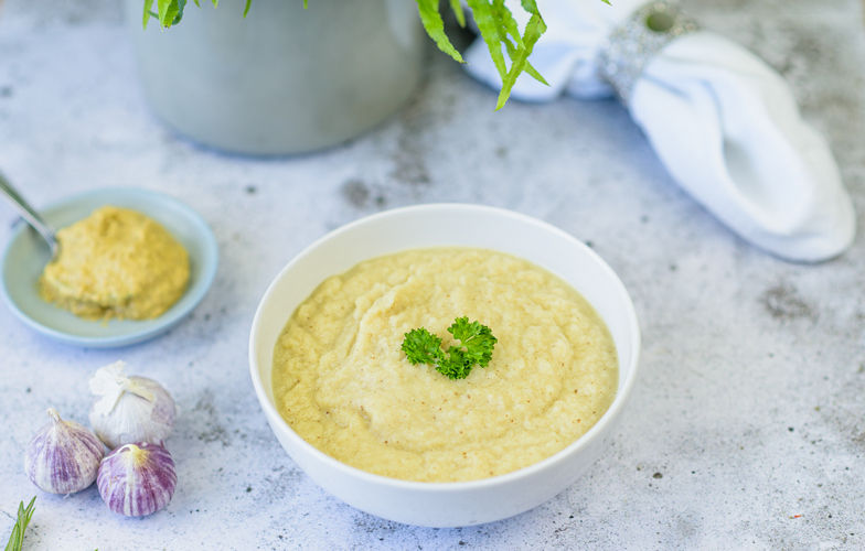 Romige knolselderij-mosterdsoep in witte kom met verse kruiden garnering