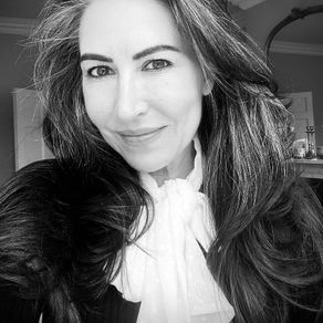 Stella Dove with long hair and a gentle smile in a grayscale image. She wears a white scarf and black top, standing in a softly lit indoor setting.