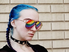 Girl with blue hair and rainbow flag reflected in her glasses
