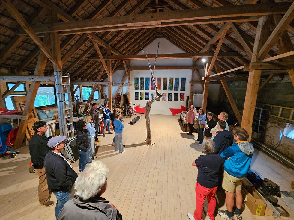 Menschen stehen im Kreis in einem Atelier-Dachstuhl, der auch Lager- und Werkstatt-Raum ist