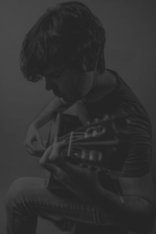 background image of guitarist Alberto Puerto seated with classical guitar