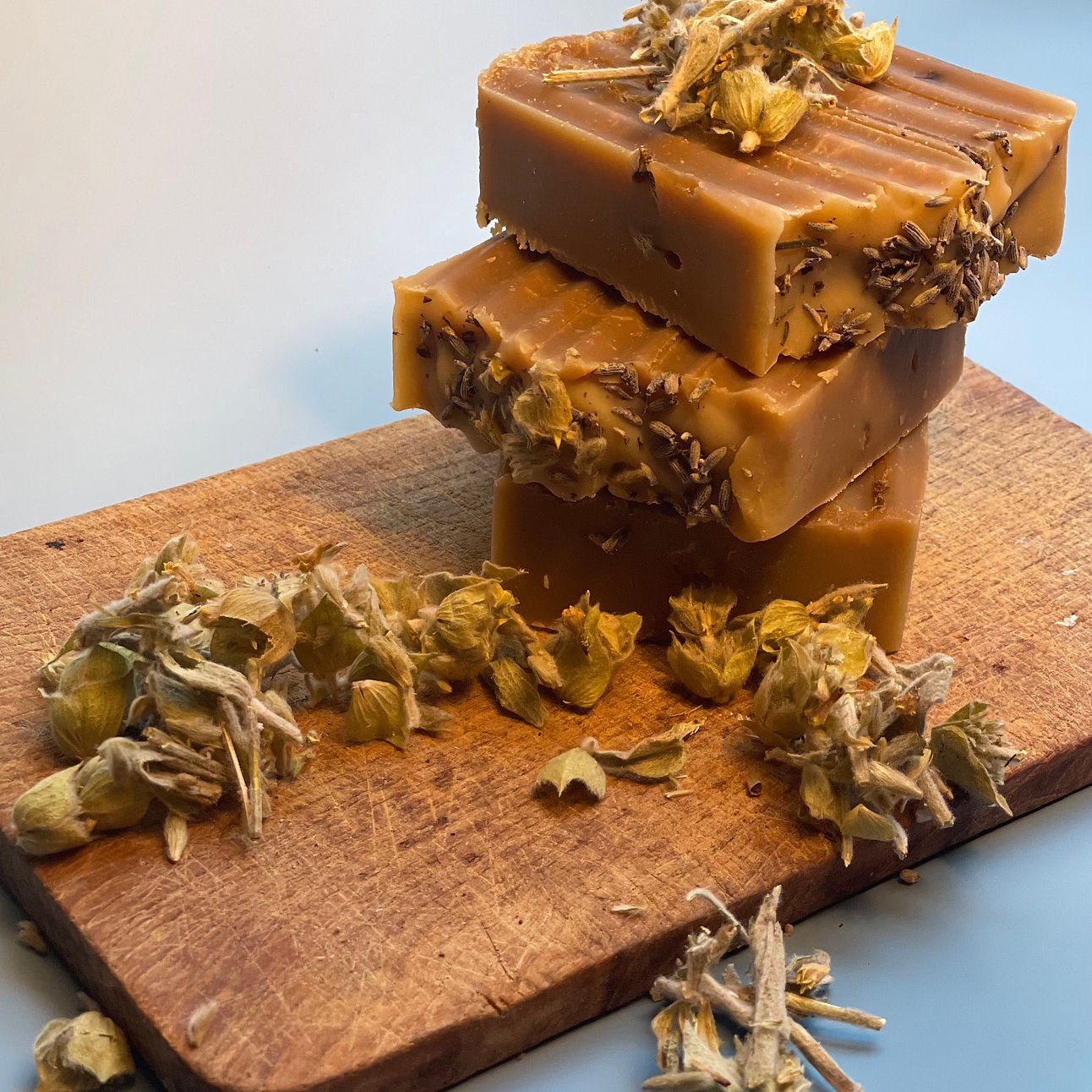a stack of soaps sitting on brown cutting board decorated and surrounded with herbs