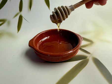 Raw honey dripping into a ceramic bowl with olive leaves, natural skincare ingredient for hydration and gentle cleansing