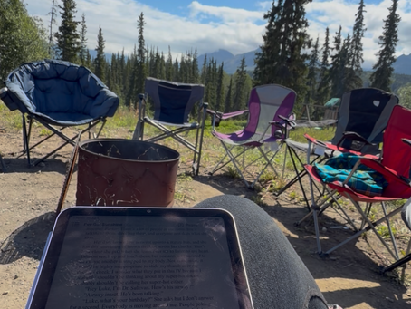 Katie working on her writing beside an Alaska campfire with her iPad