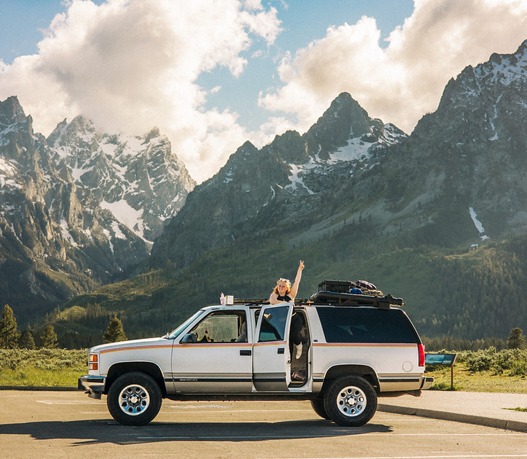 Solo Female Traveler with Converted Suburban Camper in Front of Grand Teton Mountains.