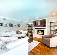 Fully Finished Basement with a sectional beige couch, hardwood floors, accent chair, bookshelves, fireplace, with wall mounted TV that was renovated by Unidos Construction