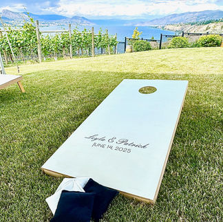 white personalized cornhole lawn game with black and white bean bags set on a lawn at a Penticton winery during a wedding