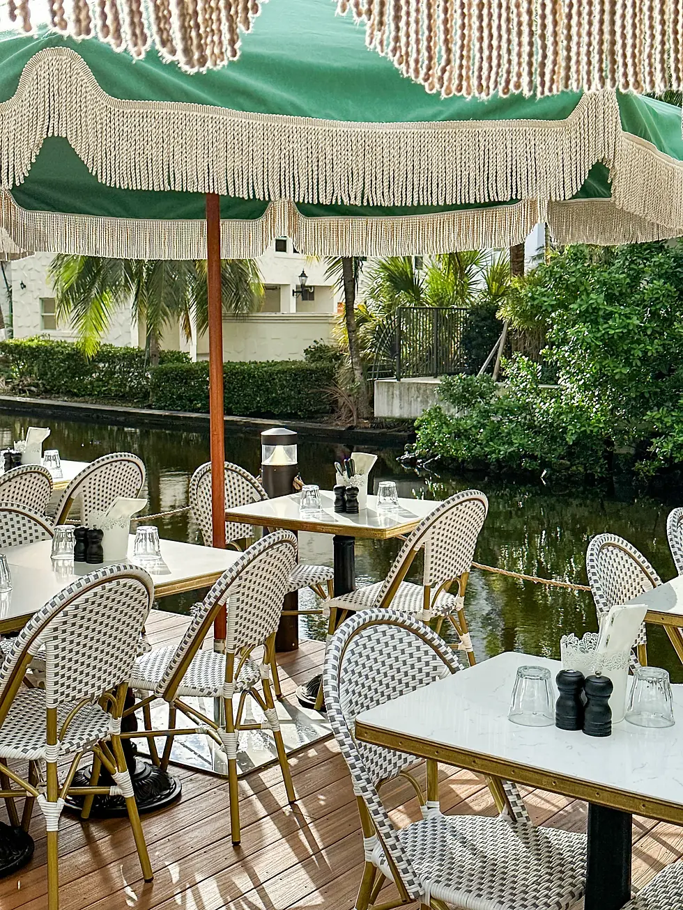 Canal-side patio at Café Bastille Fort Lauderdale with umbrella-shaded bistro tables along the Himmarshee Canal, a short walk from the Founding Families Fall Festival at Stranahan House.