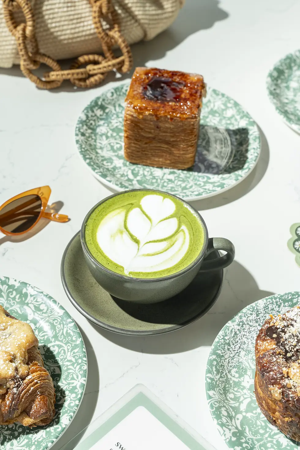 A matcha latte with leaf art, accompanied by a crème brûlée croissant on a decorative green plate at a cafe in Miami Beach