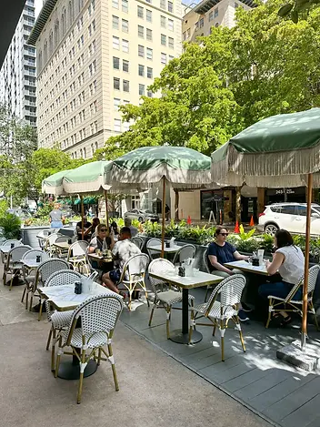 Open-air patio at Cafe Bastille Downtown Miami with green fringe umbrellas, white bistro chairs, and marble cafe tables along a Downtown Miami street