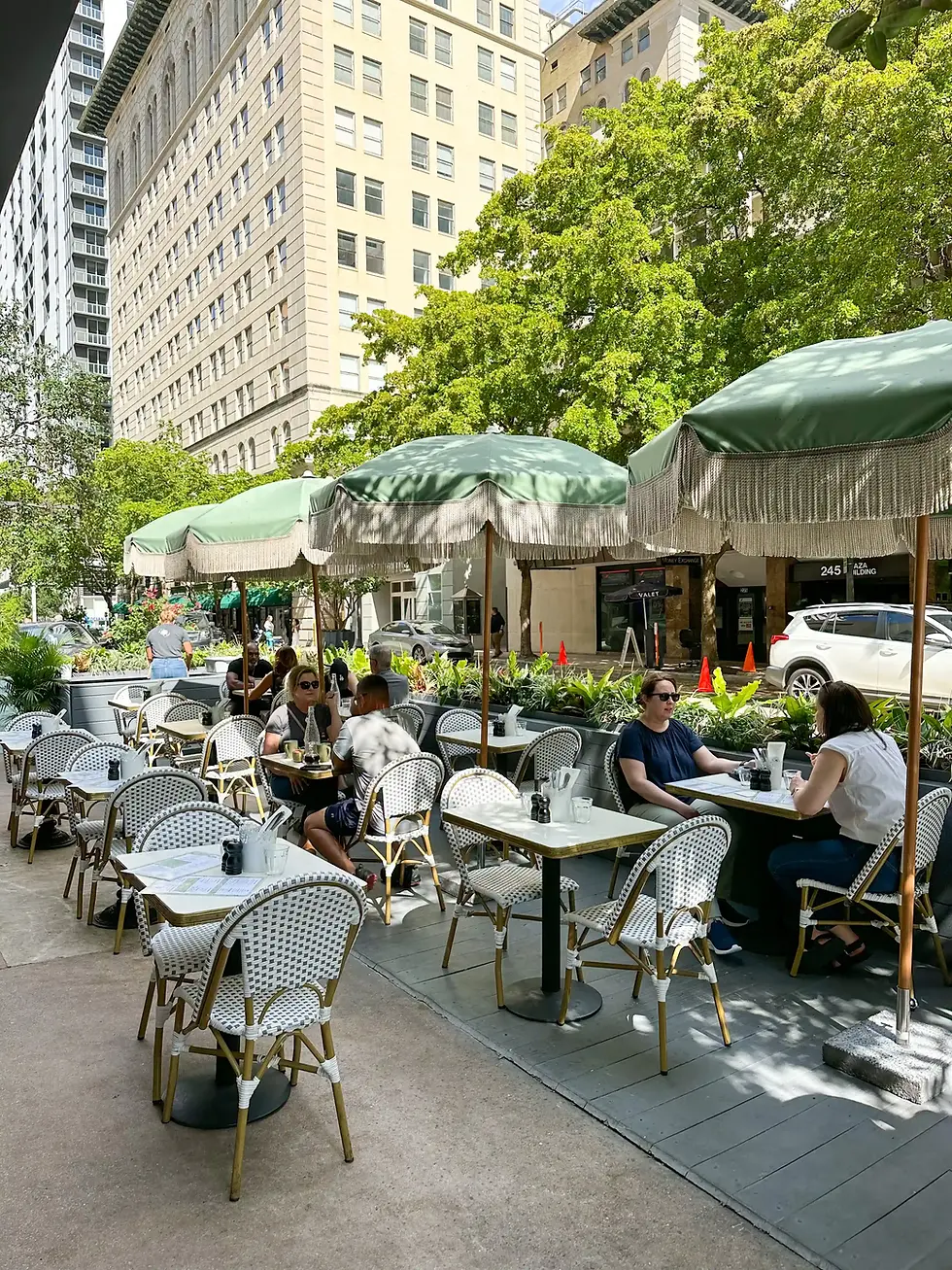 Guests dining at sidewalk patio tables under green fringed umbrellas in downtown Miami brunch