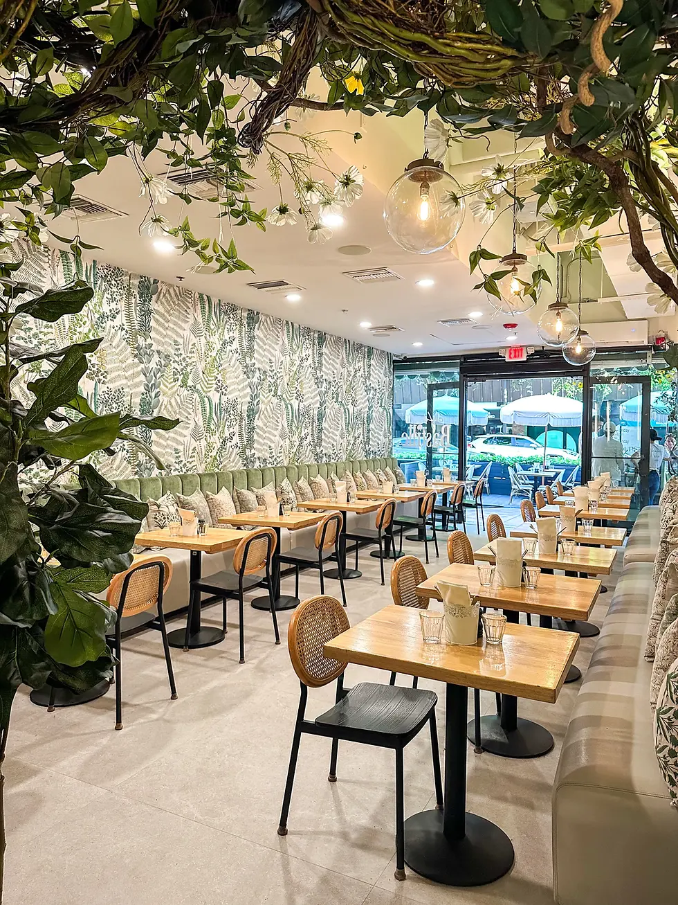 The indoor dining area with greenery, ambient lighting, and a modern design featuring tables and cushioned seating.