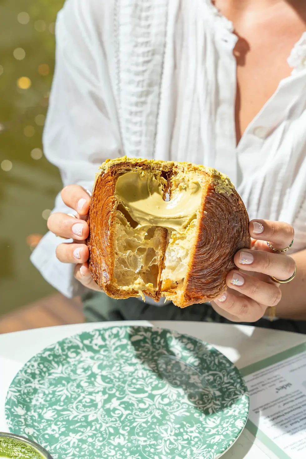 Pistachio-filled croissant split open to reveal creamy layers, served on a green plate at a sunny outdoor cafe table