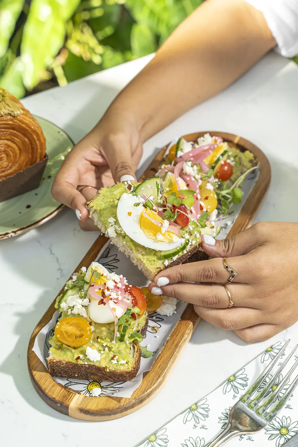 Fresh avocado toast with tomatoes, an organic egg, pickled onions, and feta oserved with red pepper flakes and cucumber