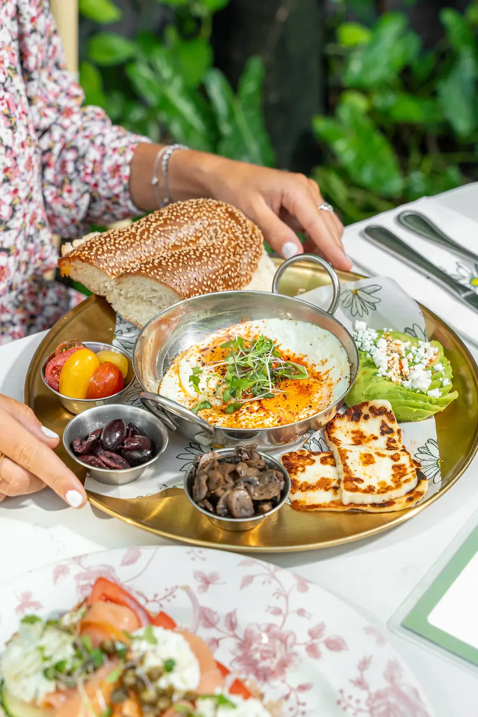 Israeli Breakfast served outdoors at a charming cafe, with eggs, grilled halloumi, olives, fresh veggies, and warm bread on a platter
