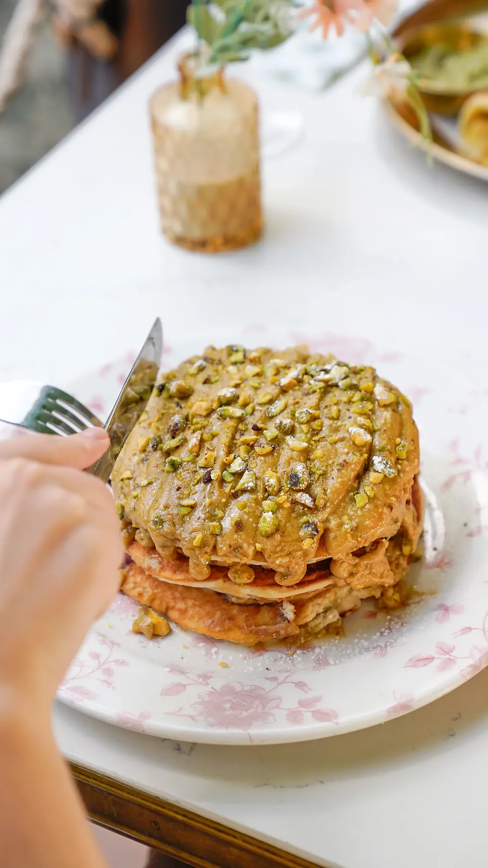 Fluffy pistachio pancakes topped with crushed pistachios, white chocolate chips, pistachio cream, and raspberry coulis.