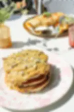 Stack of pistachio pancakes topped with pistachio cream, crumbs, and white chocolate.