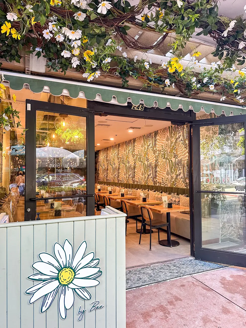 Flower-covered entrance of Café Bastille in Miami, leading to a stylish brunch restaurant interior.