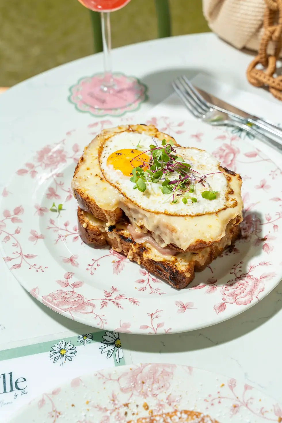Croque Madame with fried egg and melted cheese on a brioche slice, garnished with greens on a floral plate