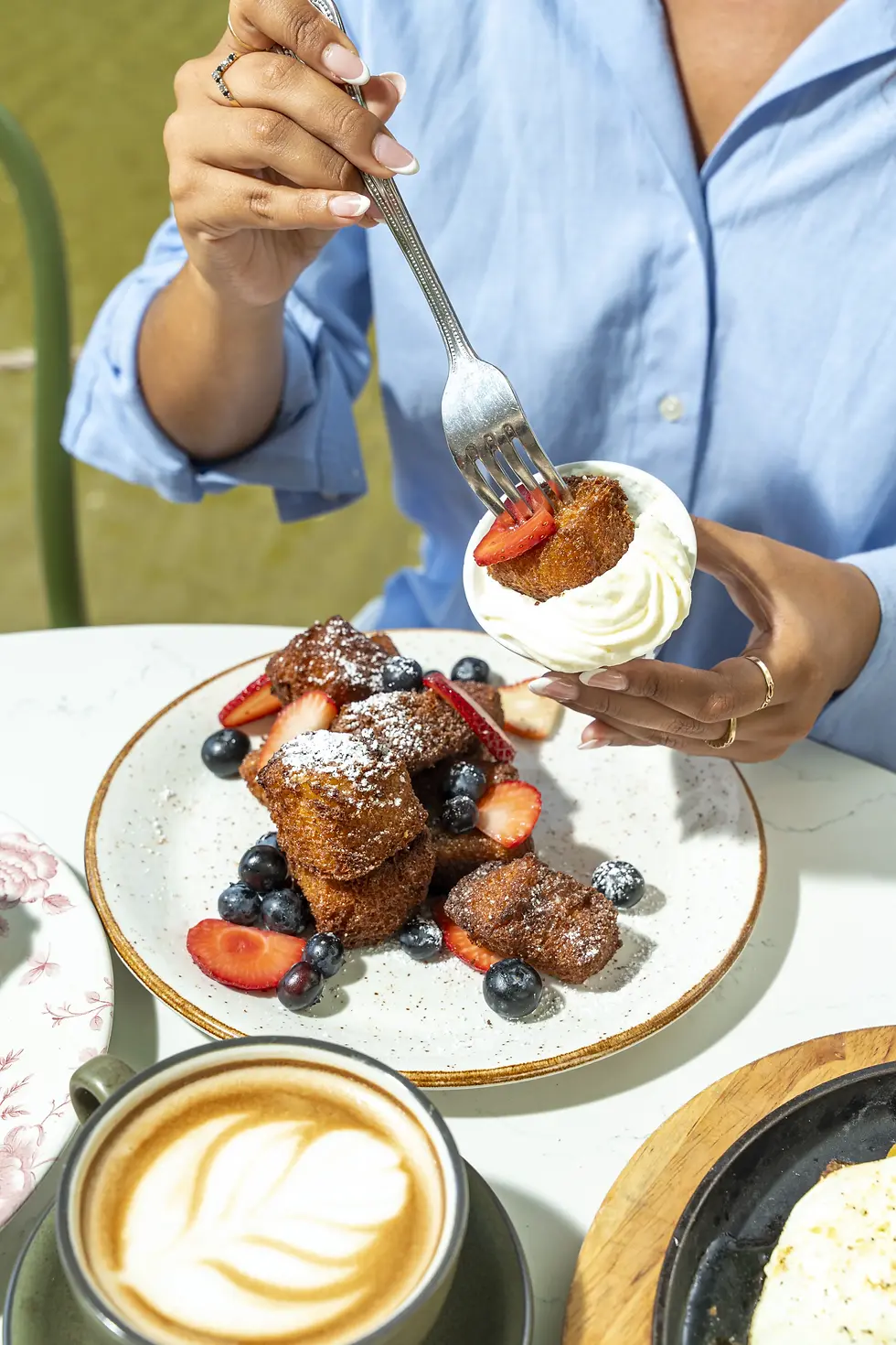 Crispy French toast bites dusted with powdered sugar, served with whipped cream, strawberries, blueberries, and a latte