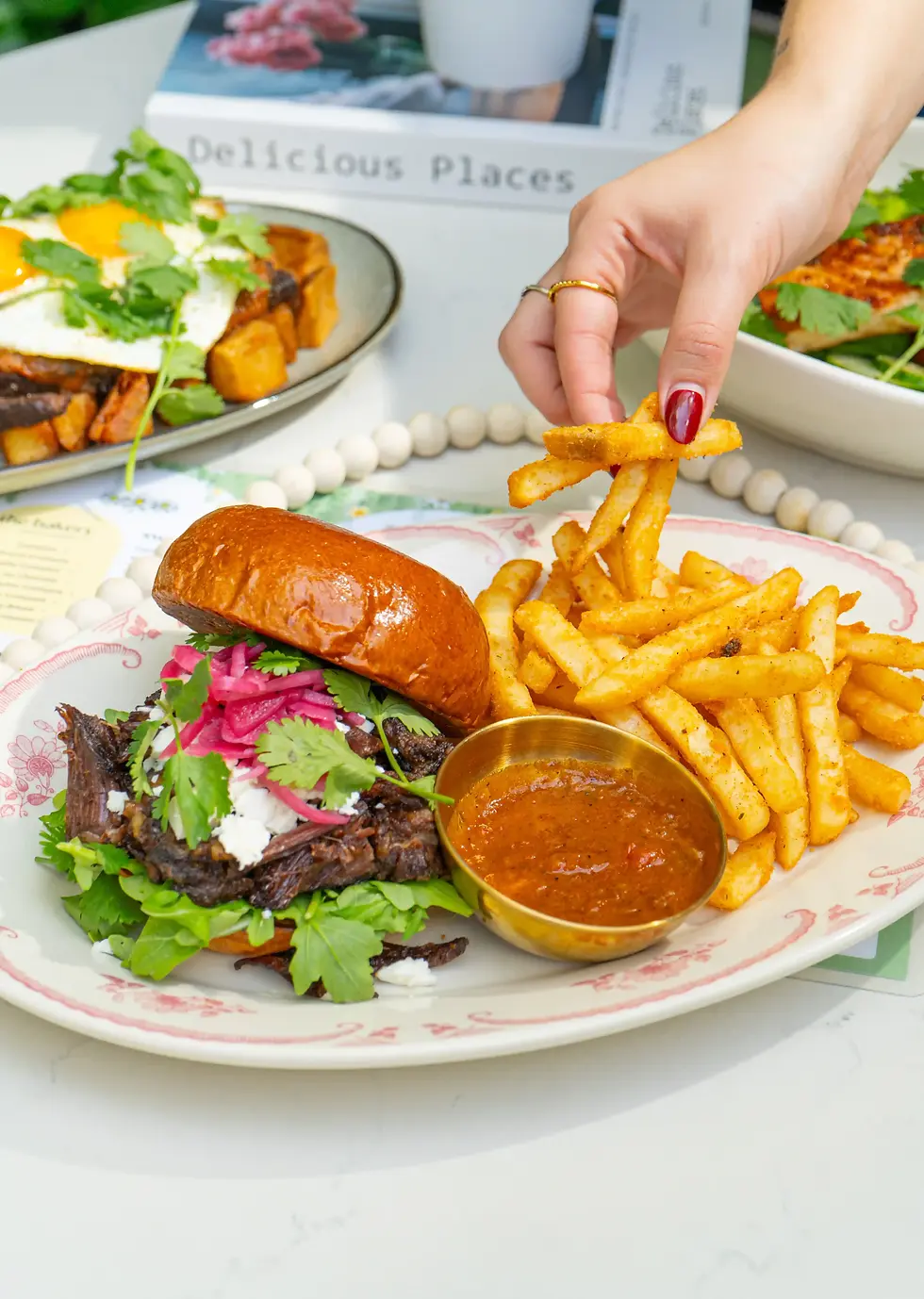 A woman reaching for golden fries next to a short rib bun topped with herbs and pickled onions at a miami brunch spot