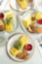 Four omelette plates with avocado, toast, and ketchup set on patterned dishes across a bright cafe table