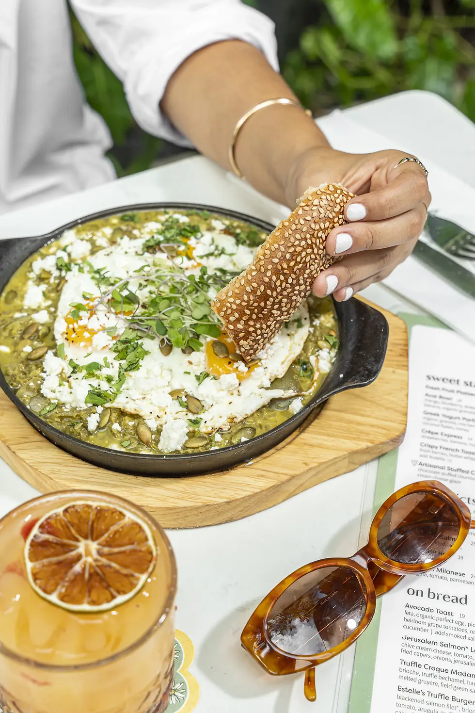 Green shakshuka with eggs and feta, served in a skillet with a refreshing drink in the background.