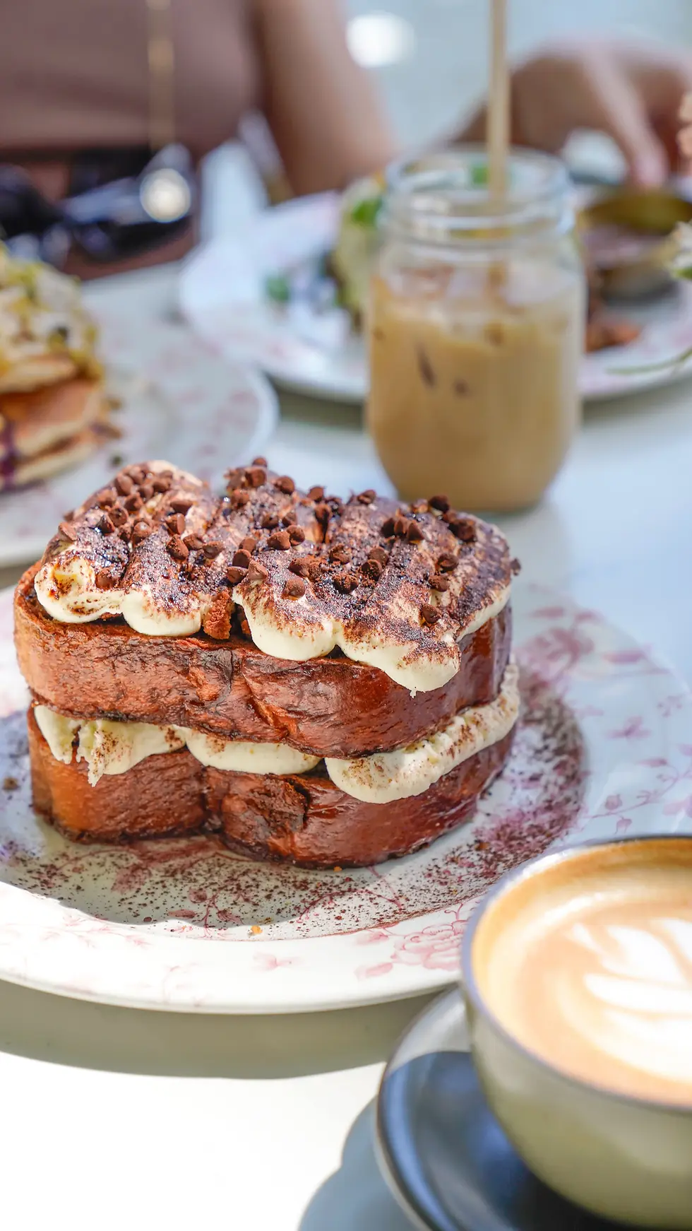 Two layers of rich Tiramisu French toast with dulce de leche cream and fresh raspberries served with coffee on a table.
