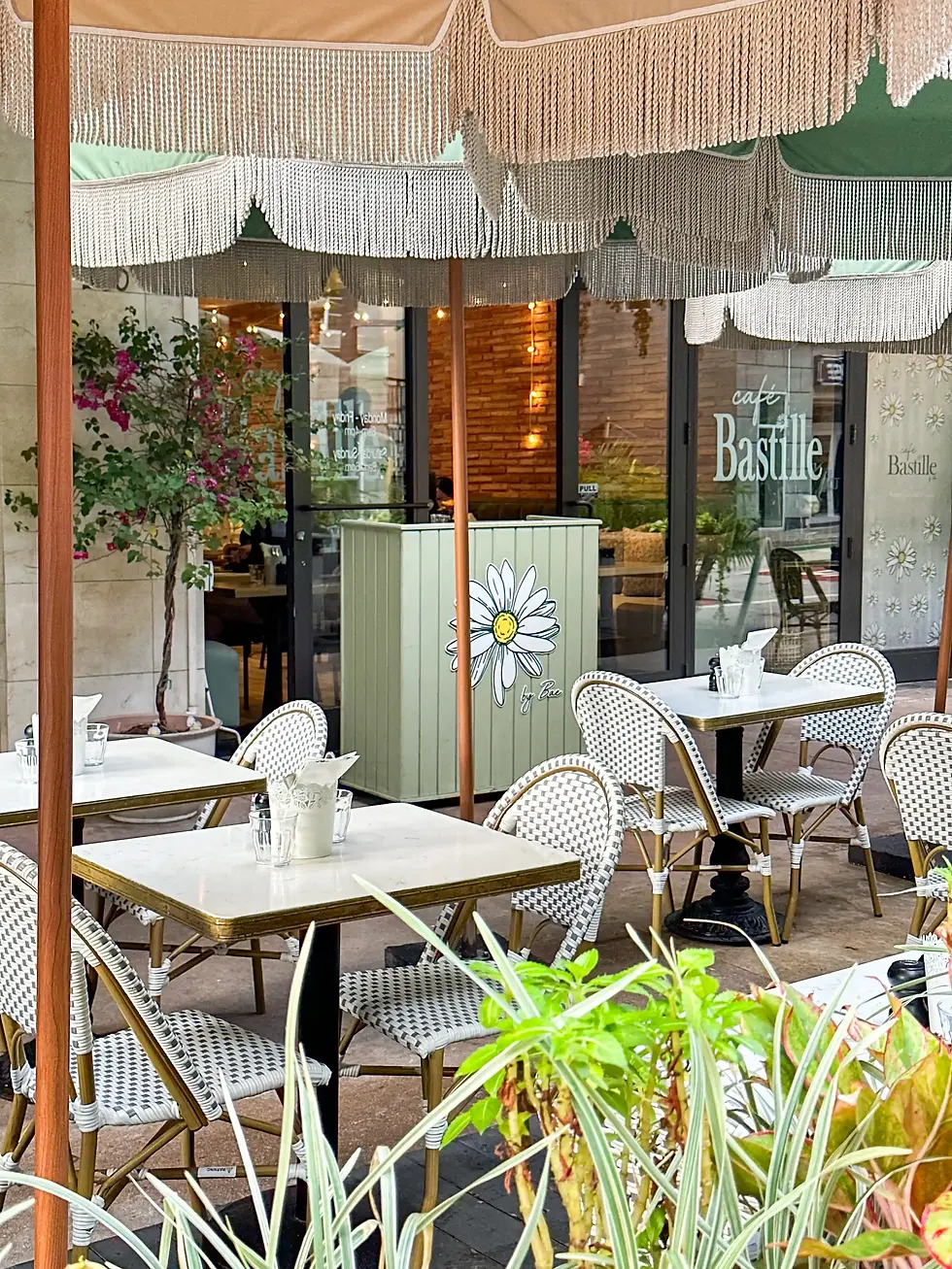 Café Bastille Fort Lauderdale interior with botanical wallpaper, sage green walls, and bistro tables under warm lighting