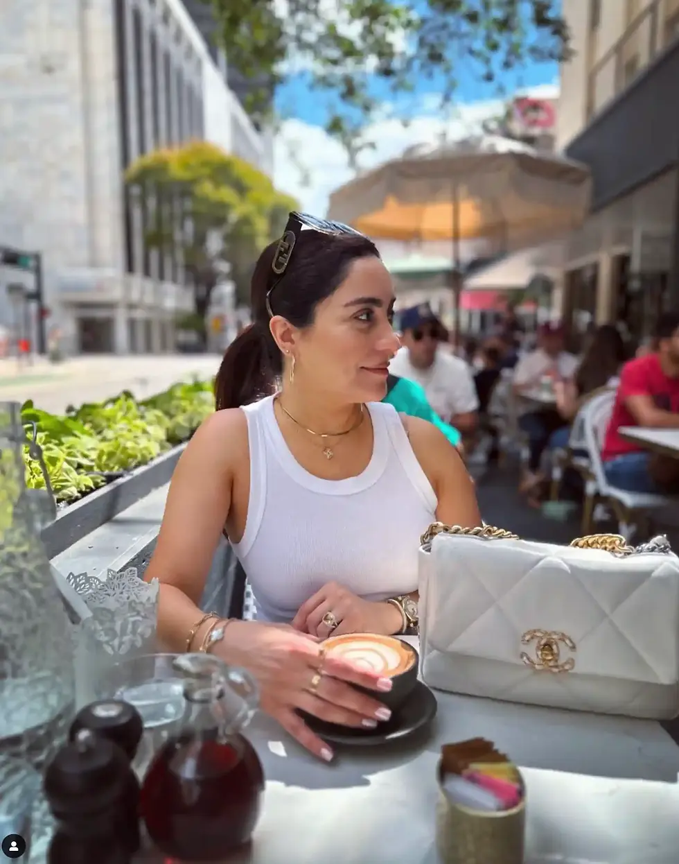 A woman sitting at an outdoor patio table holding a cappuccino at Café Bastille Downtown Miami.