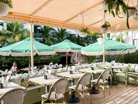 Café Bastille covered outdoor patio with mint green fringed umbrellas, wicker chairs, and hanging plants overhead 