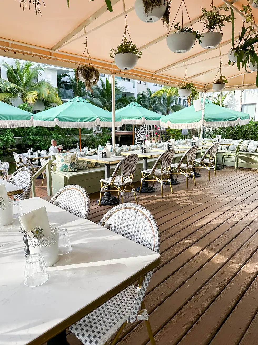 Sunlit terrace at Café Bastille with white tables and green umbrellas for the best brunch in Miami