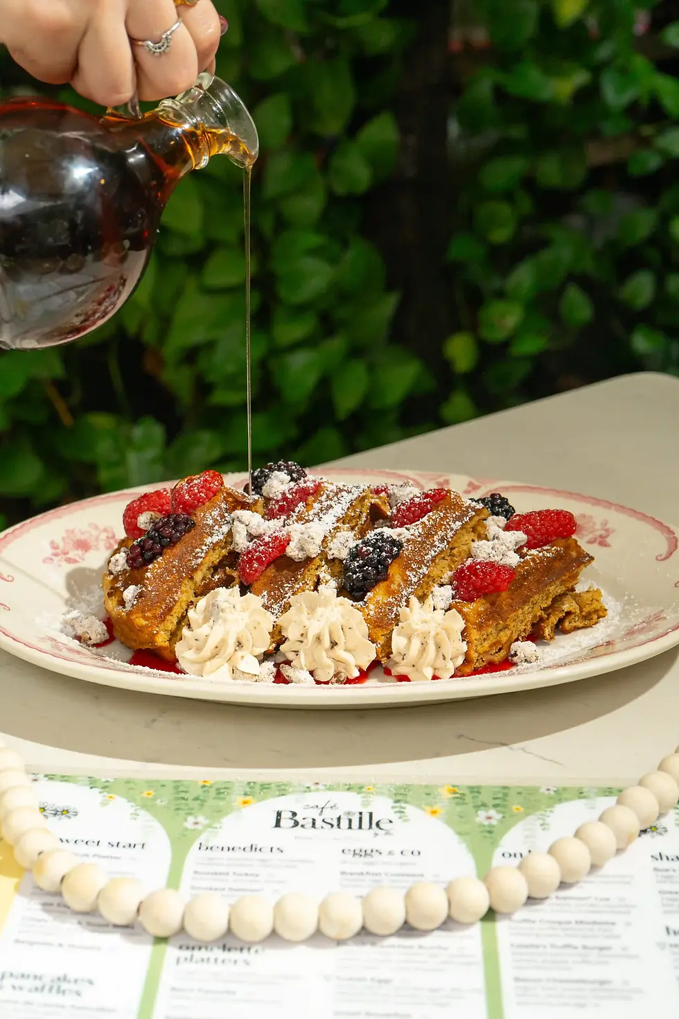 Syrup being poured over Sweet Potato Waffles topped with berries and powdered sugar, at the best brunch in Miami