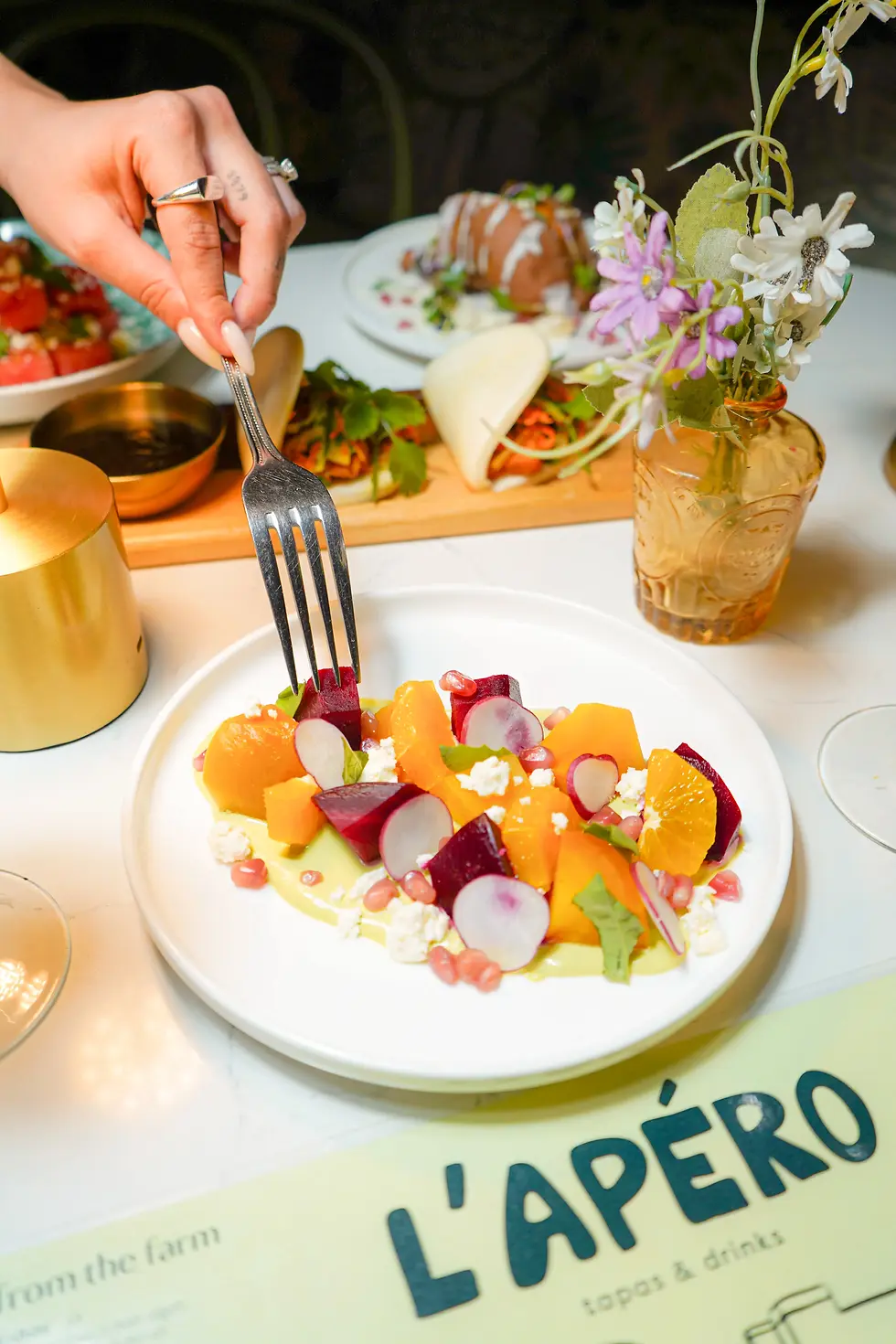 A plate of beets with orange, herbed goat cheese, pomegranate, served with other dishes and drinks.