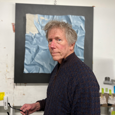 Artist Otto Duecker stands in front of one of his paintings wearing a black turtleneck.