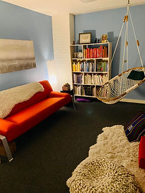 a cozy office space with a couch, pillows, bookshelf and hammock chair.