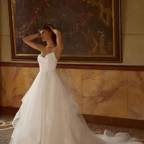 Strapless ball gown with satin bodice and tulle ruffle skirt. Featuring a ruched bodice that creates a pointed sweetheart neckline. Horsehair defines hem of each tier on skirt. Complete with satin covered buttons extending to end of chapel length train.