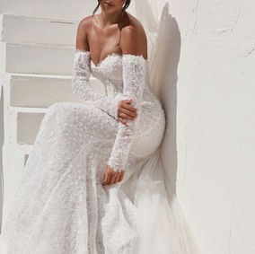 Effortlessly blending tradition with modern allure, Style 1860 catches every eye down the aisle with its sexy design and exquisite couture details. Detachable long sleeves, finished with fabric-covered buttons at the wrists, complement a strapless sweetheart neckline bodice with exposed boning, both adorned with delicate eyelash lace trim. The allover lace column silhouette, embellished with 3D florals, sequined accents and pearl embellishments over glittering tulle hugs every curve, ensuring a radiant descent down the aisle. Sparkling details and captivating design combine for a one-of-a-kind sexy column wedding dress.