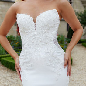 Capturing the romance and beauty of timeless bridal design, Style D3853 features a flattering column silhouette of graphic lace appliqu and crepe. The strapless sweetheart neckline plunges into the embellished lace-adorned bodice and seamlessly meets a sheer open back detail with a gown-length row of vintage-inspired pearl buttons. Stretch crepe fabric melts over the figure to meet a glitter tulle cutout train of delicate lace applique to complete this romantic wedding dress.