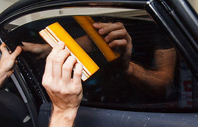 Master installs a tint film for the car glass with a hairdryer and spatula with glare of l