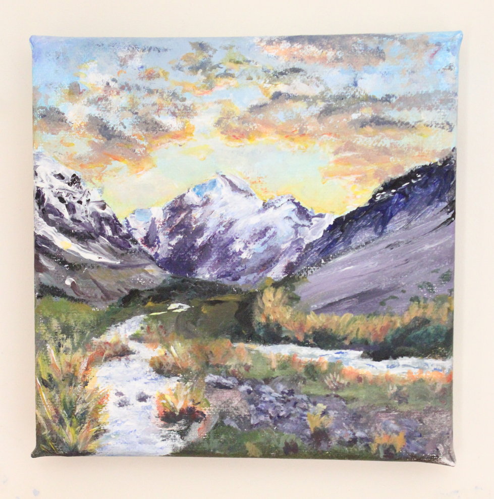 This painting feels like a quiet breath drawn deep in the wilderness. Towering snow-capped peaks stretch across the horizon, their violet and white tones softened by a dreamy, sun-kissed sky of amber, peach, and gold—hinting at the hush of dawn or the hush before dusk. Below, a winding river glides through a richly colored valley, framed by trees in full autumnal flourish—greens, rusts, and hints of coral foliage adding warmth to the scene.
The composition invites the eye to follow the river inward, almost as if it’s leading to a secret kept by the mountains themselves. It’s peaceful but alive—like nature holding its breath in that golden, fleeting hour