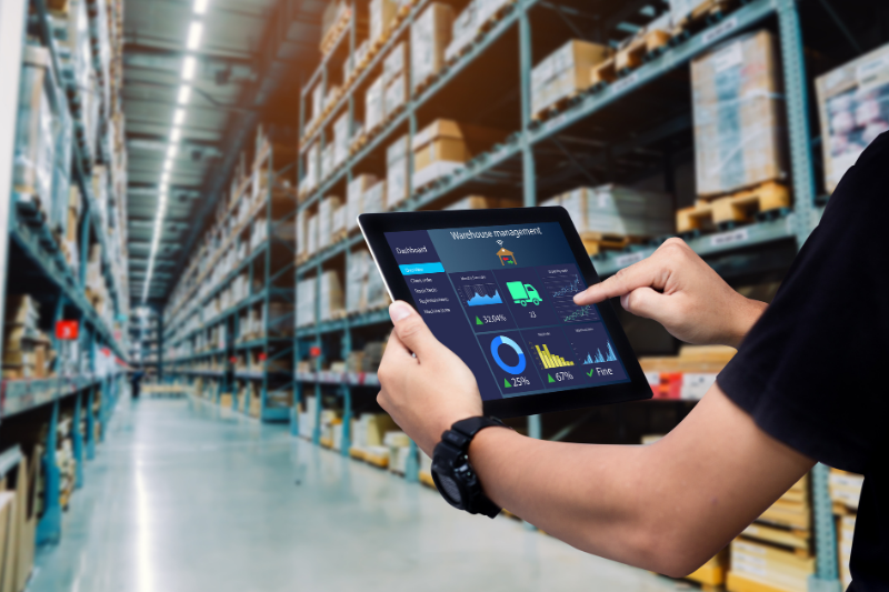 Person using a warehouse management dashboard on a tablet in a large fulfillment center.