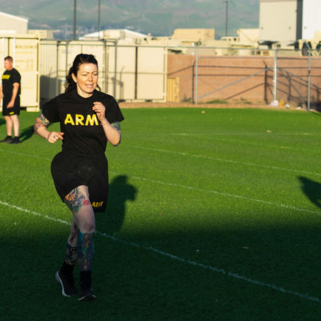 A woman in army PT gear running on a grassy field. 