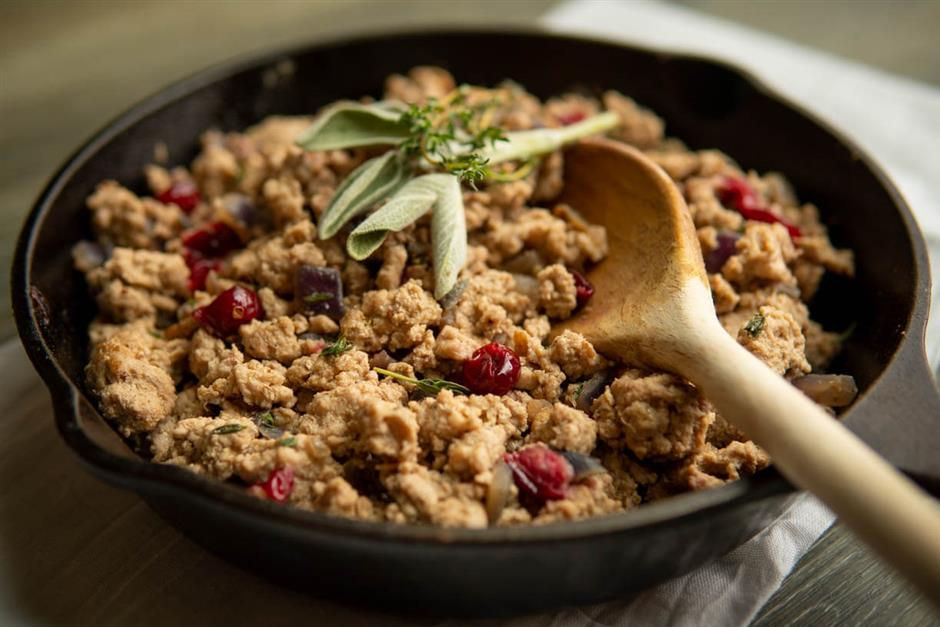 A skillet with stuffing featuring cranberries, herbs, and bread chunks, with a wooden spoon resting inside. Earthy tones and rustic mood.