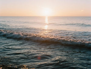 Ocean waves at sunrise with soft light and water reflections.