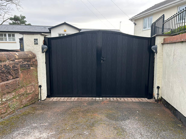 Driveway gate with a black powder-coated finish and black composite wood infills, featuring a swan-neck bend across both gates.