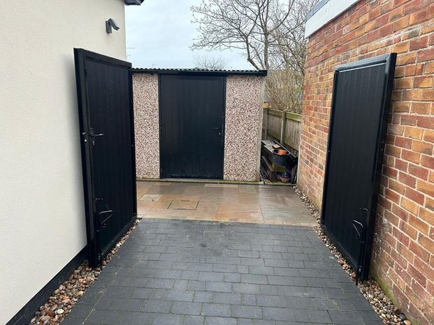 Black gates open to reveal a garage, surrounded by brick and concrete.