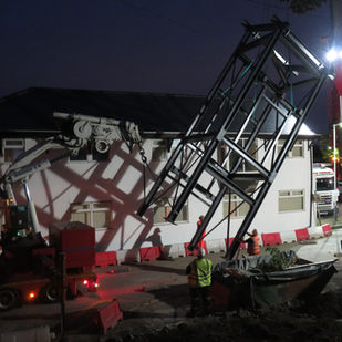 a large metal structure is being lifted in front of a building with a crane that says ' dingo ' on it